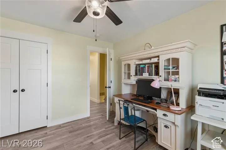 Wood-finish flooring, white panel doors with black hardware, and a ceiling fan with integrated lighting