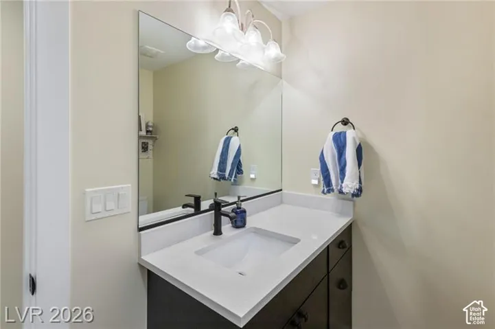 Vanity with dark wood-finish cabinetry, integrated rectangular sink, light-toned countertop, and wall-mounted mirror with overhead lighting