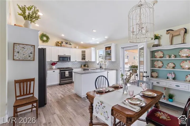 Vaulted ceiling with recessed lighting, white cabinetry, subway tile backsplash, kitchen island with granite countertop, and wood-finish flooring
