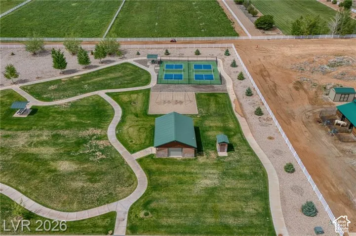 Expansive green space featuring multiple paved pathways, a covered picnic area, two tennis courts, a sports court, and a recreation building