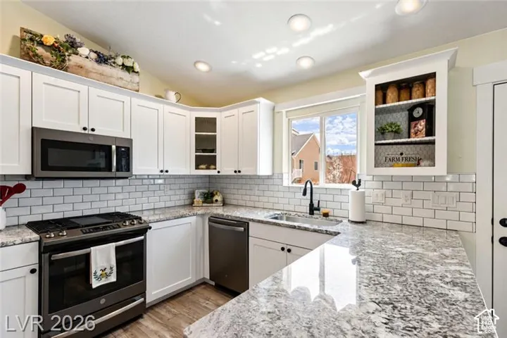 White cabinetry with dark hardware, stainless steel appliances, speckled stone countertops, subway tile backsplash, and wood-finish flooring