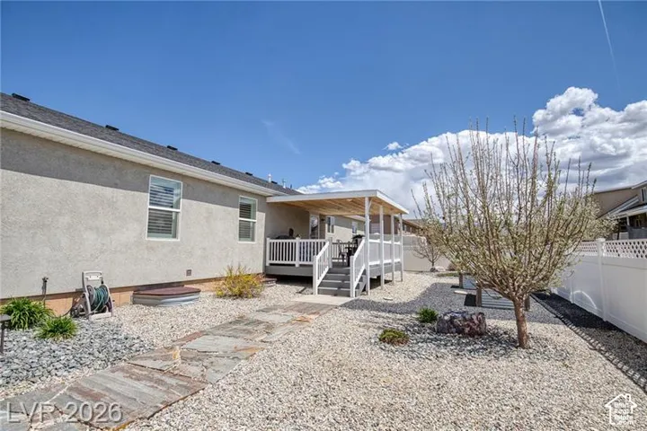 Rear exterior featuring a covered deck, white privacy fencing, and a stone walkway