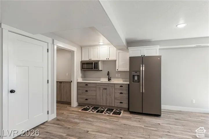 Contemporary kitchen featuring white shaker upper cabinetry, wood-finish lower cabinetry, light-toned countertops, and a full-size stainless steel refrigerator
