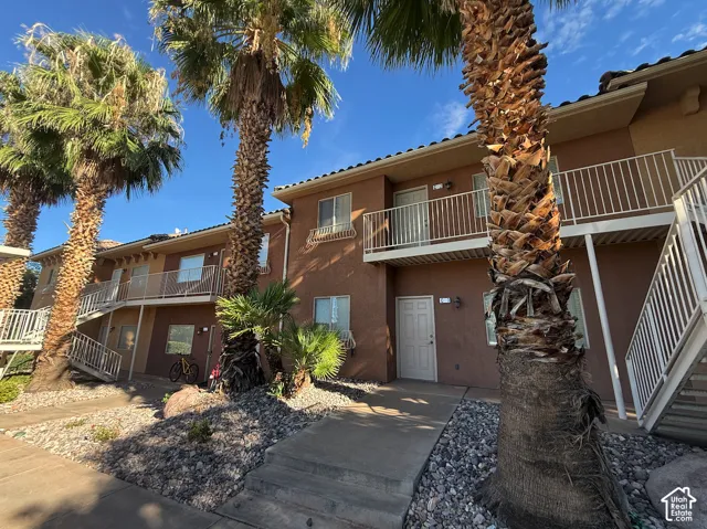 Two-story building with a stucco exterior, multiple balconies with white railings, and mature palm trees