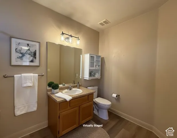 Vanity with an integrated sink and laminate countertop, wood-finish flooring, wall-mounted light fixture, and a built-in wall cabinet