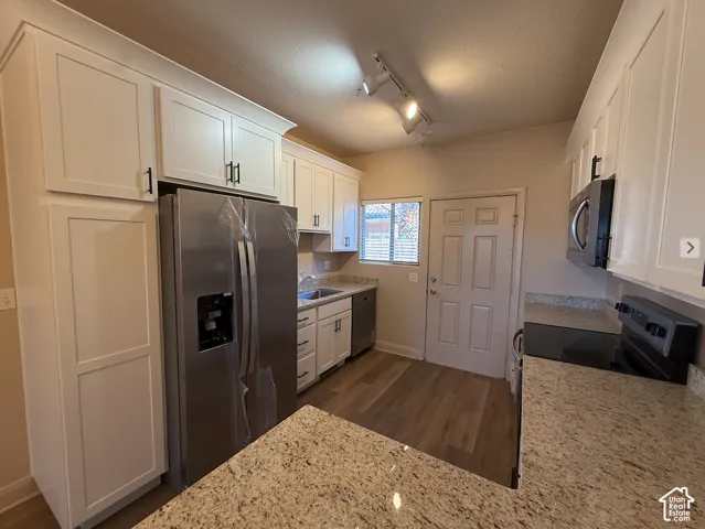 White shaker cabinetry with crown molding, stainless steel appliances, speckled stone countertops, wood-finish flooring, and track lighting
