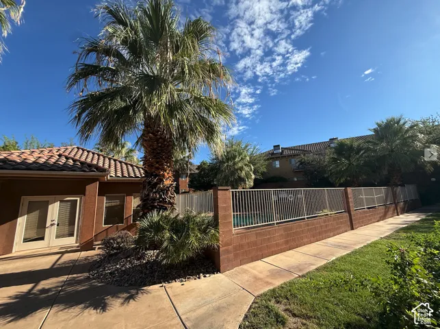 Terracotta tile roof with stucco exterior, double glass panel doors, paver patio, and mature palm trees