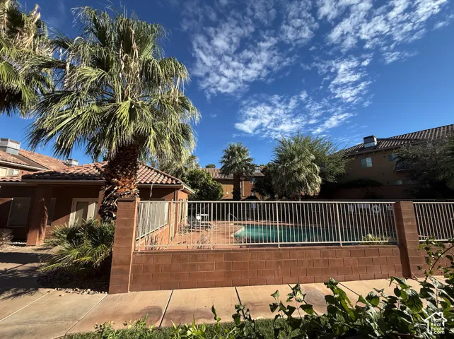 Community pool area featuring a perimeter fence, surrounding foliage, and stucco exterior buildings