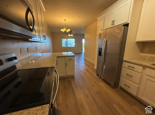 Kitchen with white cabinetry, granite-style countertops, stainless steel appliances, and wood-finish flooring