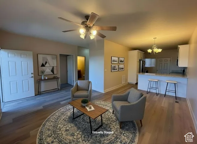 Open-concept living space featuring wood-finish flooring, a ceiling fan with integrated lighting, and a breakfast bar with stone-look countertop