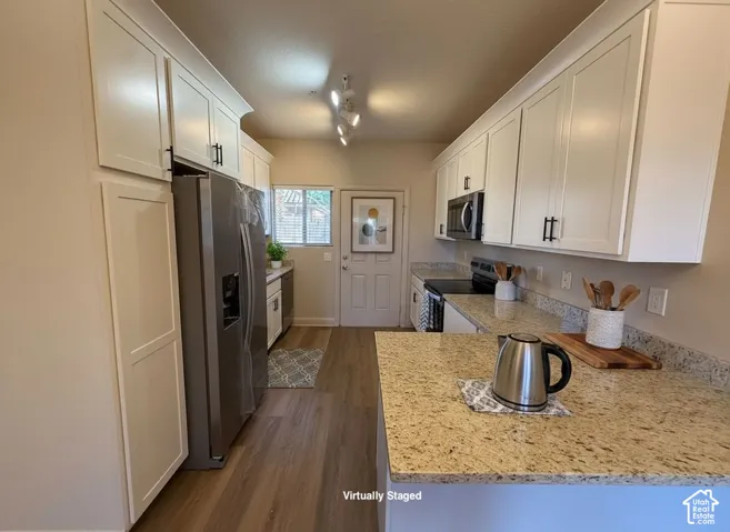 White cabinetry with black hardware, wood-finish flooring, light-colored countertops, stainless steel refrigerator, and built-in microwave