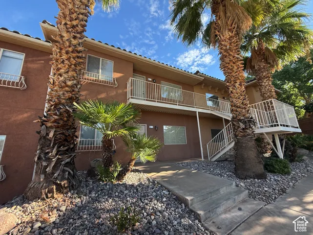Two-story building with a stucco exterior, multiple private balconies, exterior stairs, and a low-maintenance gravel landscape