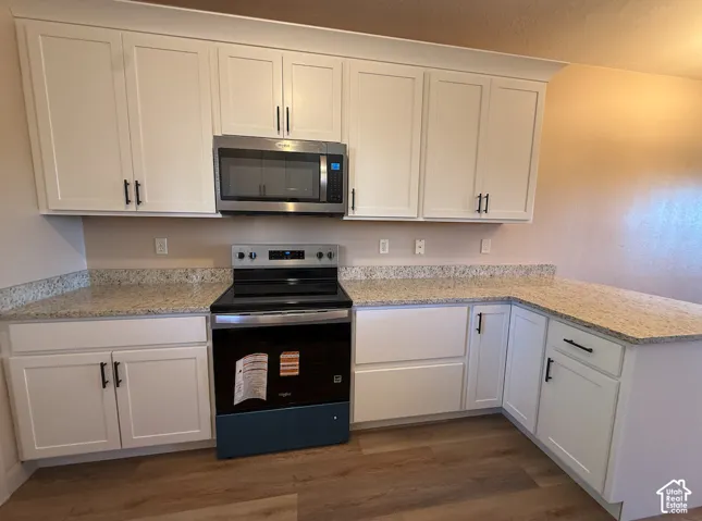 White shaker-style cabinetry with matte black hardware, granite-look countertops, stainless steel microwave, and a black electric range