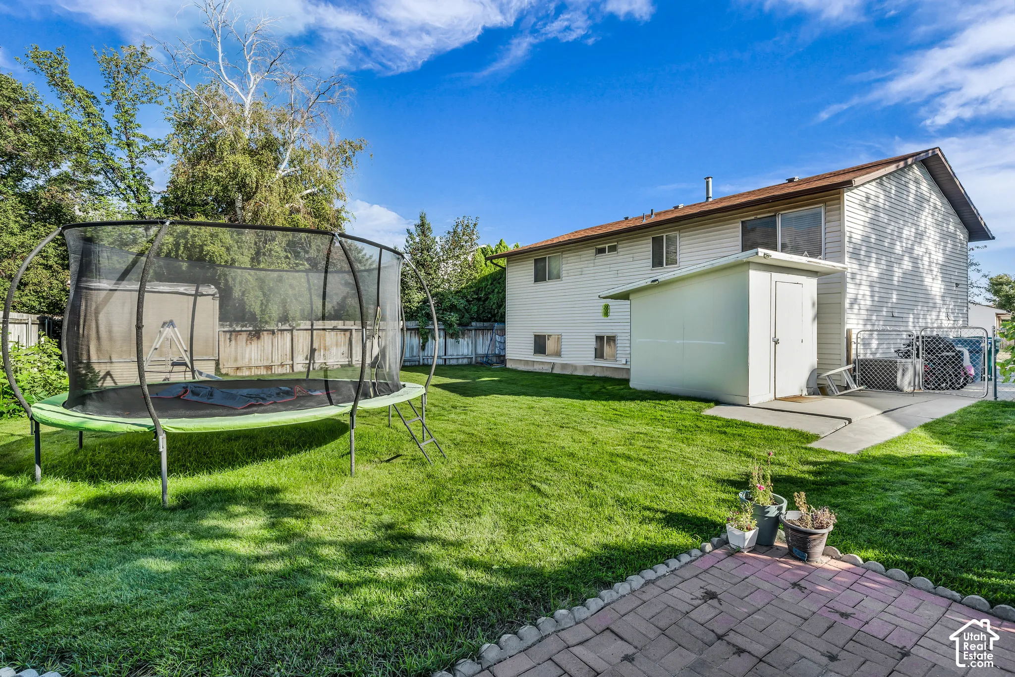 Expansive backyard featuring a manicured lawn, established perimeter fencing, a concrete patio, and an additional storage shed