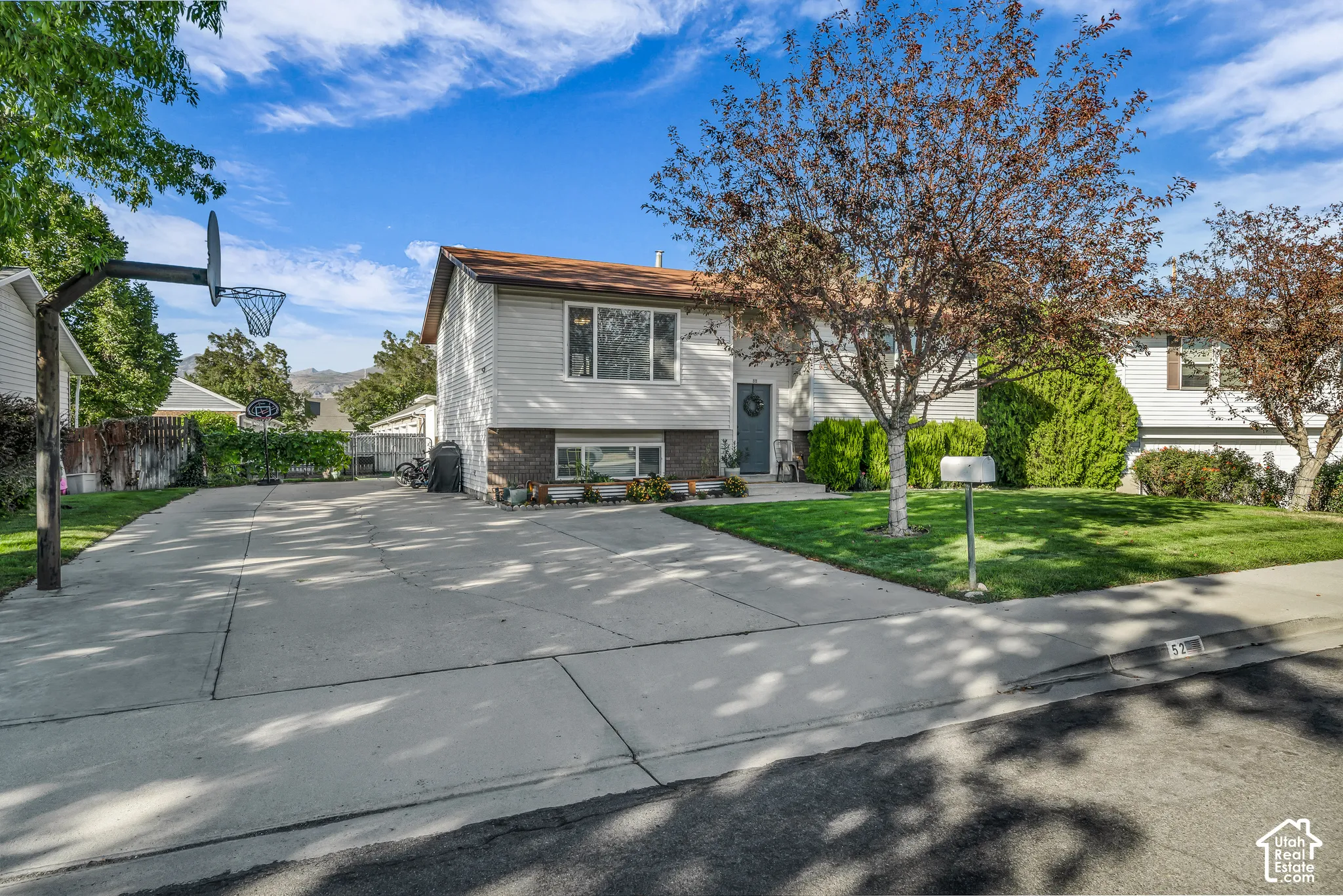 Split-level residence featuring light-colored siding and a brown roof with plenty of driveway parking