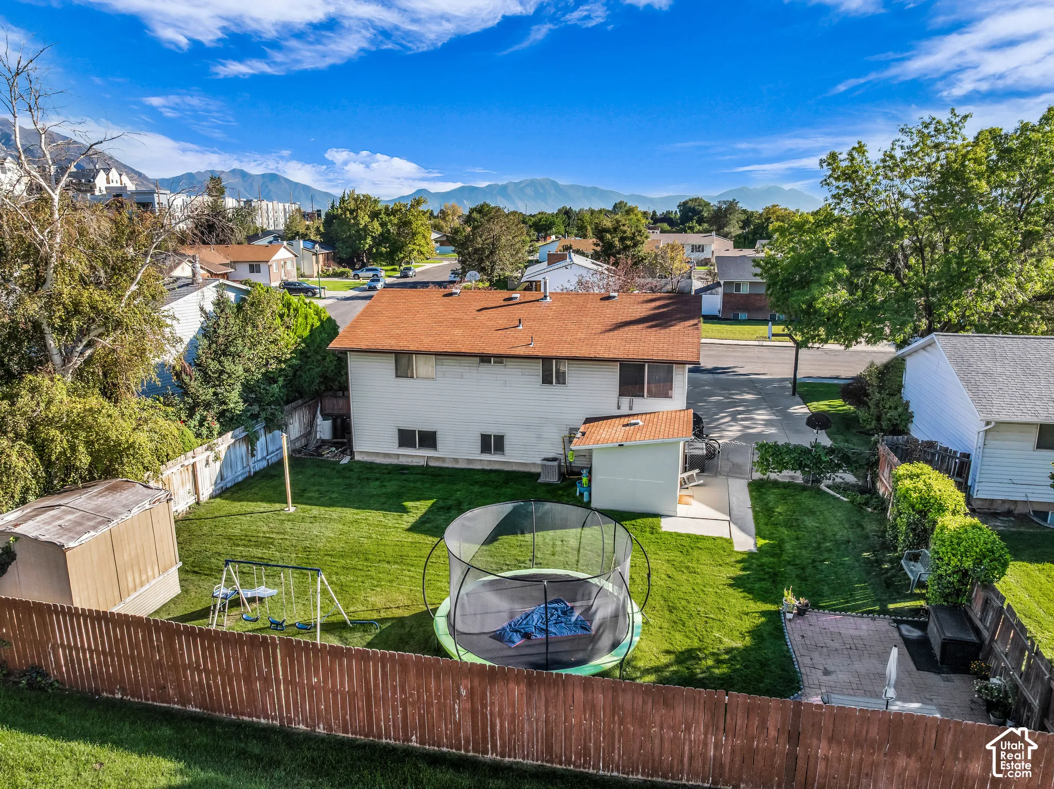 Expansive fenced backyard featuring a manicured lawn, two storage sheds, and a paved patio area