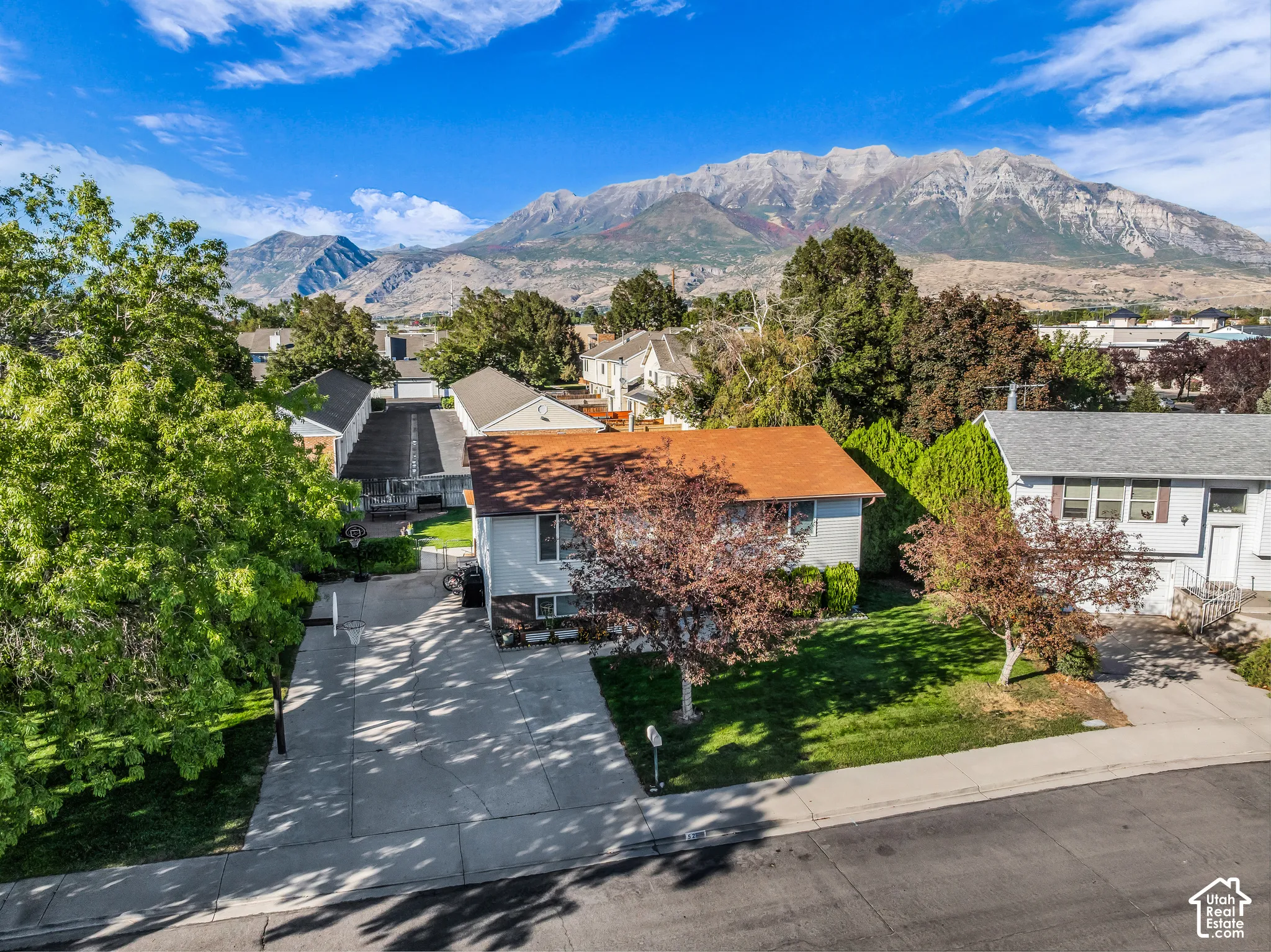 Mountain backdrop with residential properties, mature trees, and a concrete driveway