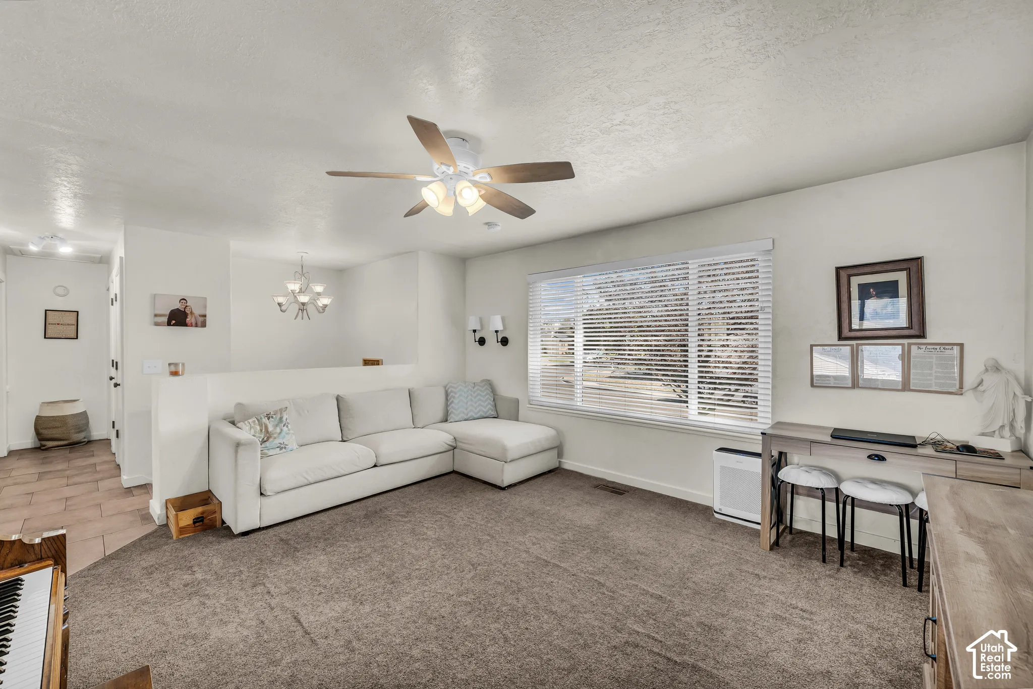 Carpeted living area featuring a large window, ceiling fan with integrated lighting, and a partial wall separating spaces