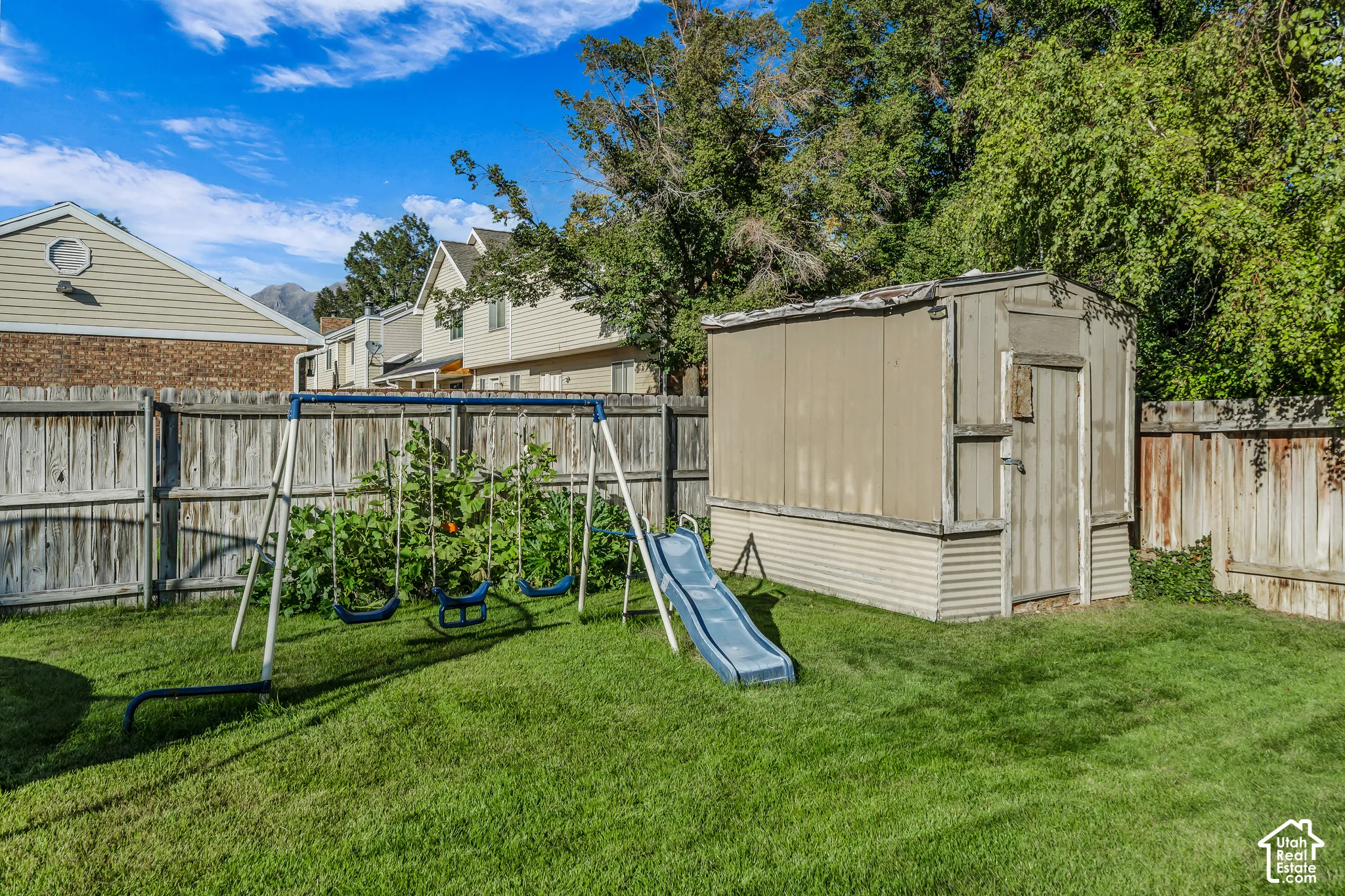 Grassed backyard with swing set, garden boxes, and a detached storage shed