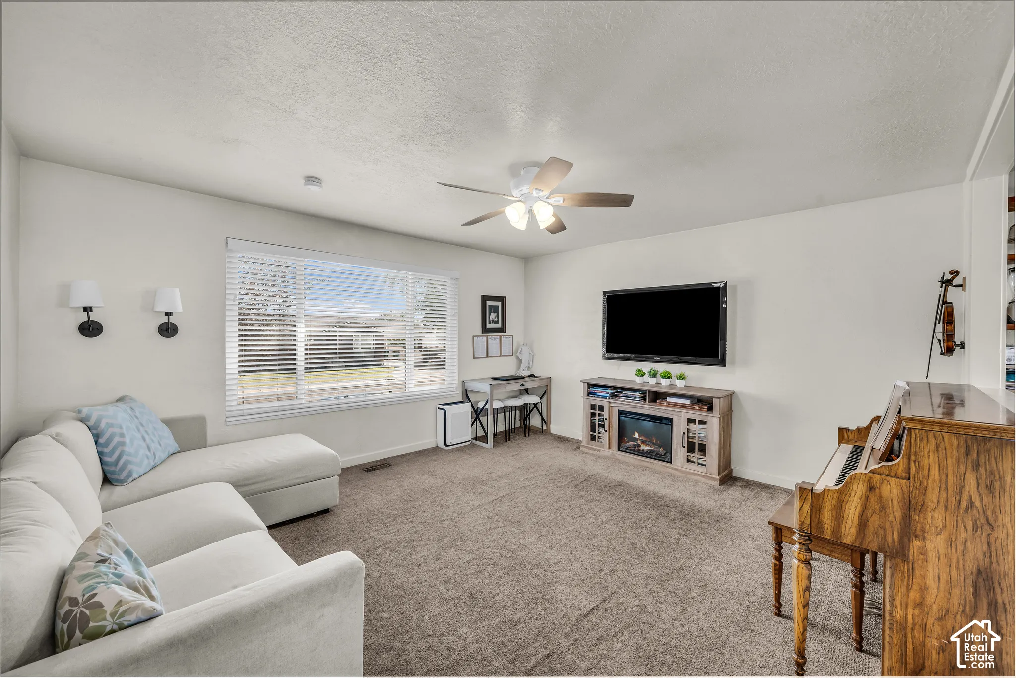 Spacious living area featuring neutral carpet, a large window with blinds, and a ceiling fan