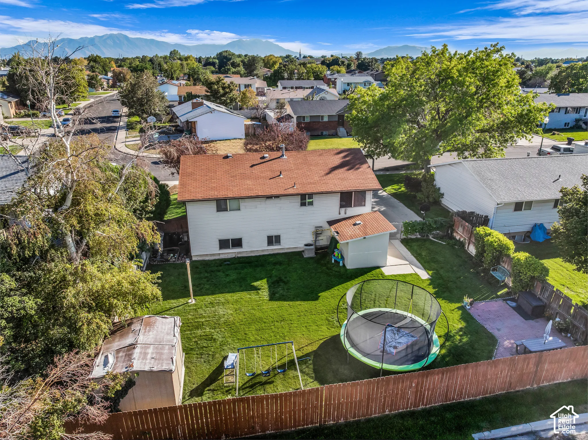 Expansive backyard featuring a manicured lawn, two storage sheds, a privacy fence, and a concrete patio area