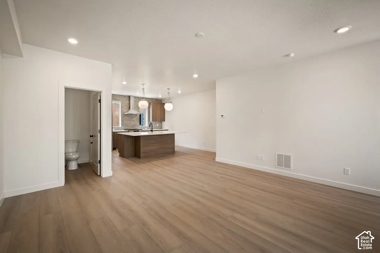 Open-concept living space featuring wood-finish flooring, recessed lighting, and a kitchen with an island, pendant lighting, and stainless steel appliances
