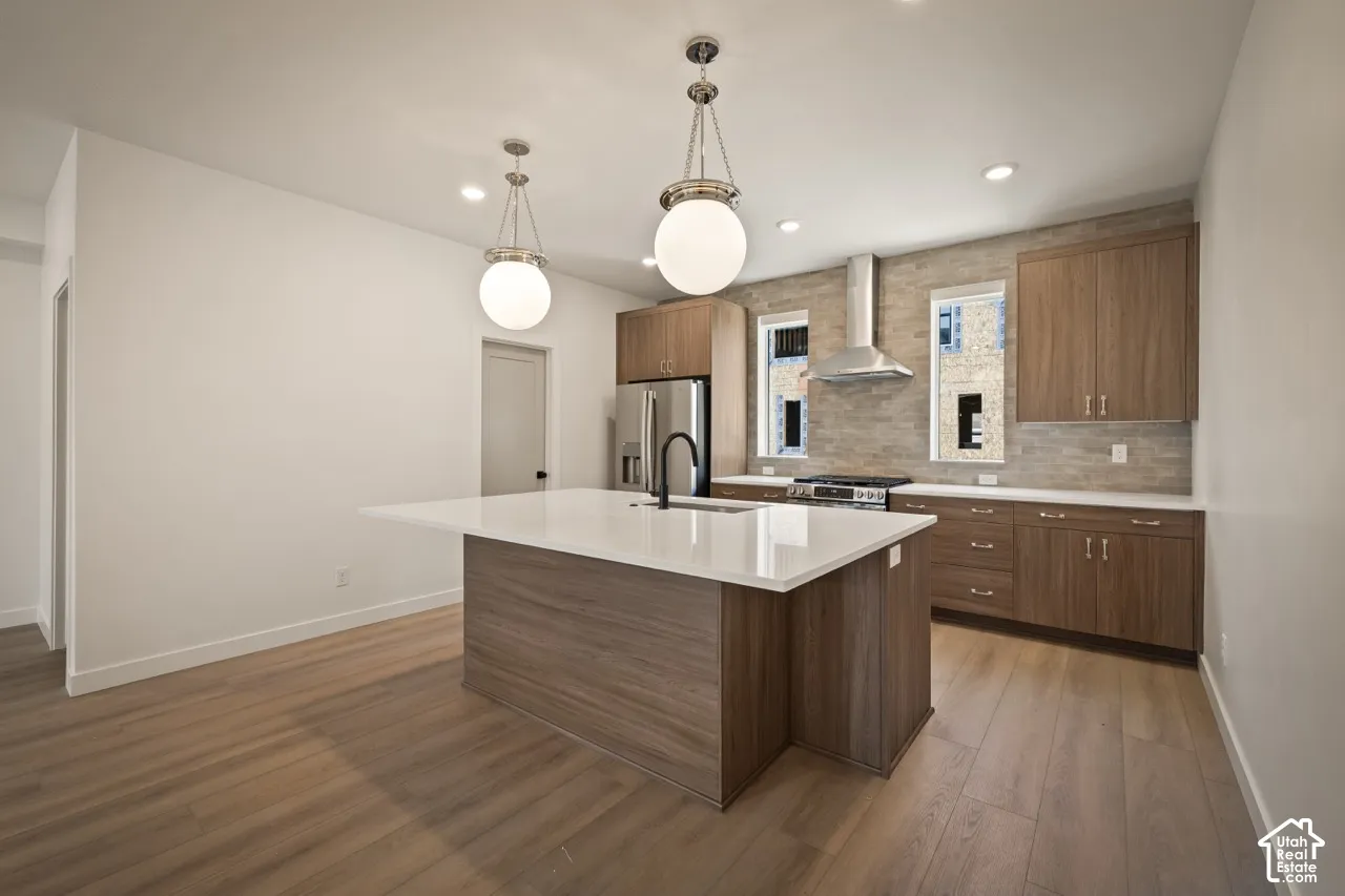 Kitchen featuring wood-finish flooring, a center island with a white countertop, wooden cabinetry, a stainless steel refrigerator, and a stainless steel range hood