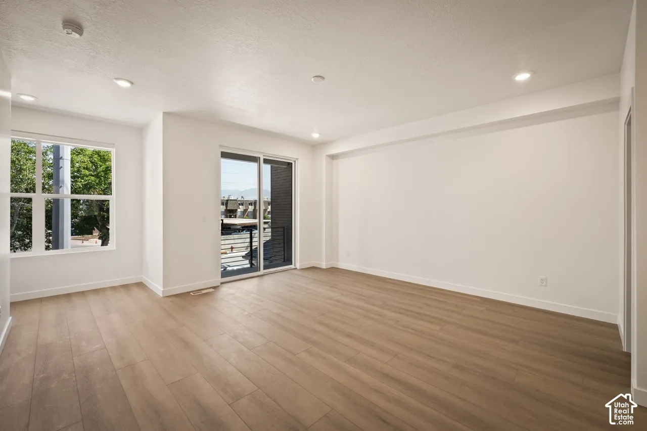 Recessed lighting with a flat white ceiling, wood-finish flooring, and a sliding glass door providing access to an exterior balcony