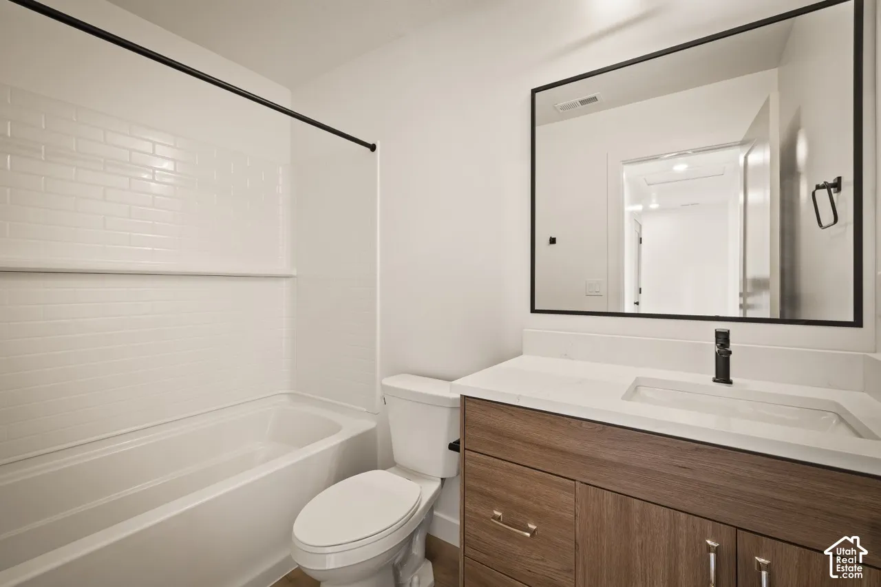 Bathroom featuring a white subway tile tub surround, built-in bathtub, toilet, wood-finish vanity with an integrated sink, and a black-framed mirror