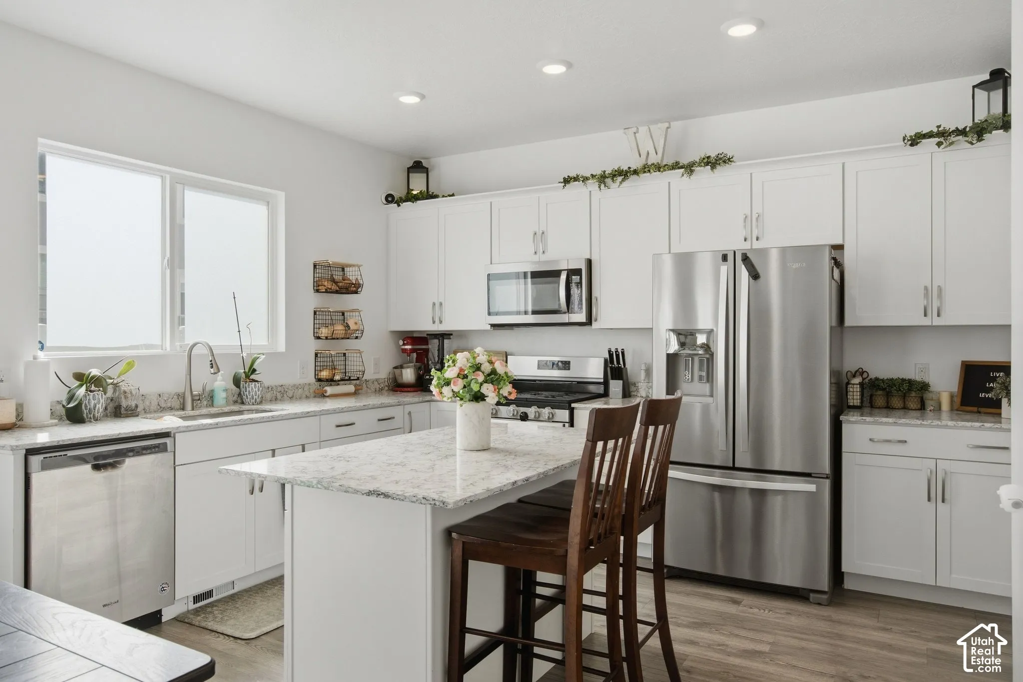 Bright kitchen featuring white cabinetry, stainless steel appliances, a kitchen island with seating, ample countertop space, and wood-finish flooring