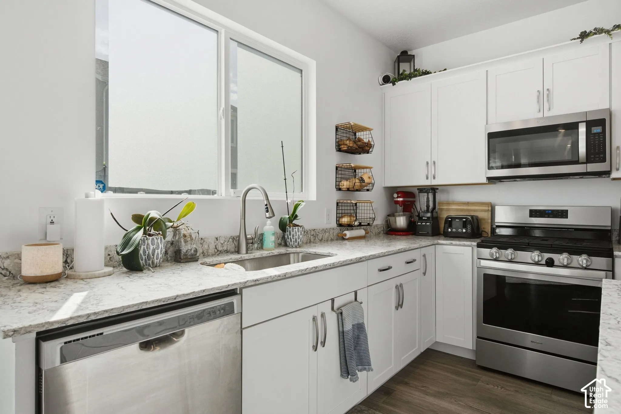 Kitchen featuring white cabinetry, light-toned countertops, stainless steel appliances, and wood-finish flooring