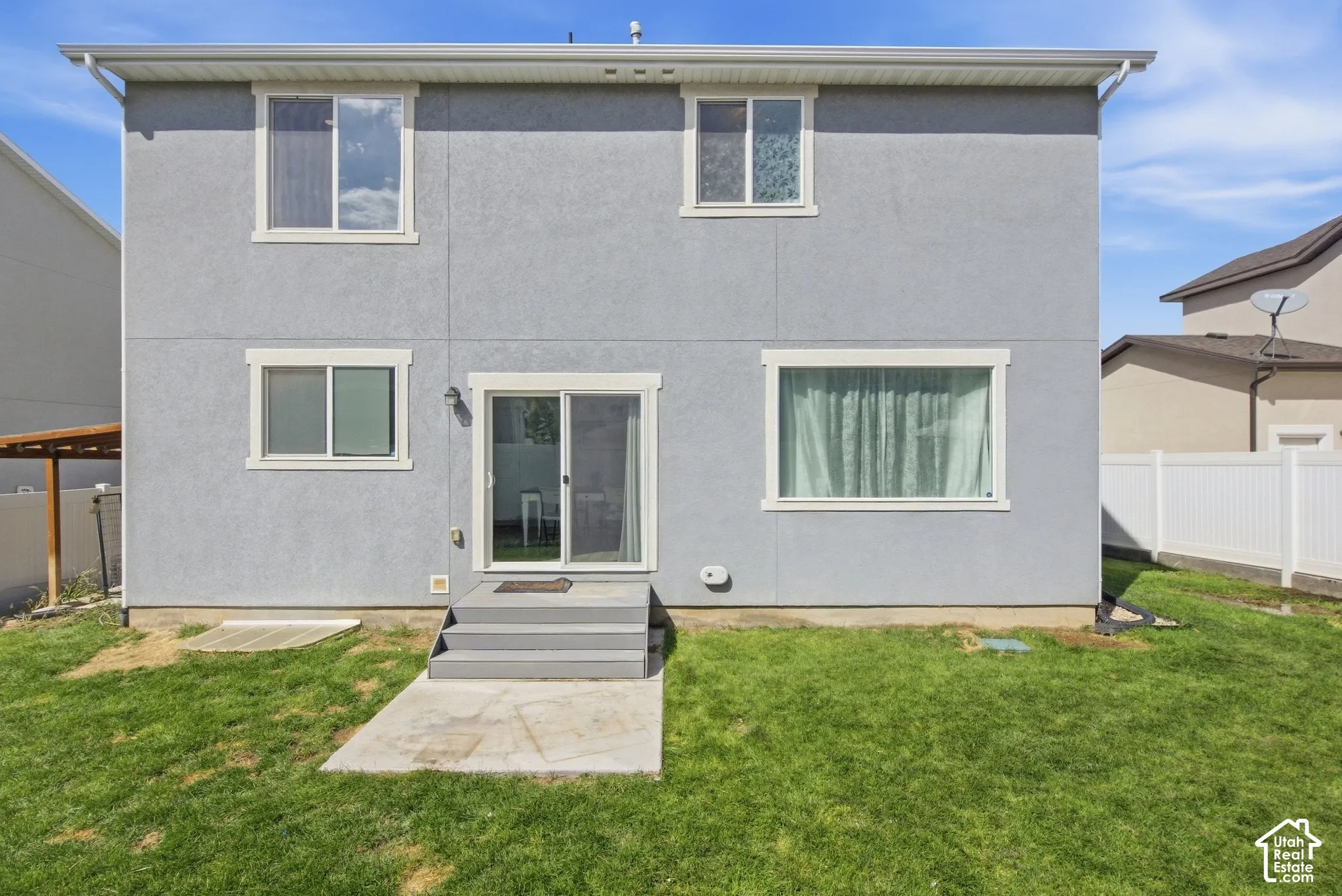Gray stucco exterior with white trim windows and sliding glass door, leading to a concrete patio and a grassy yard