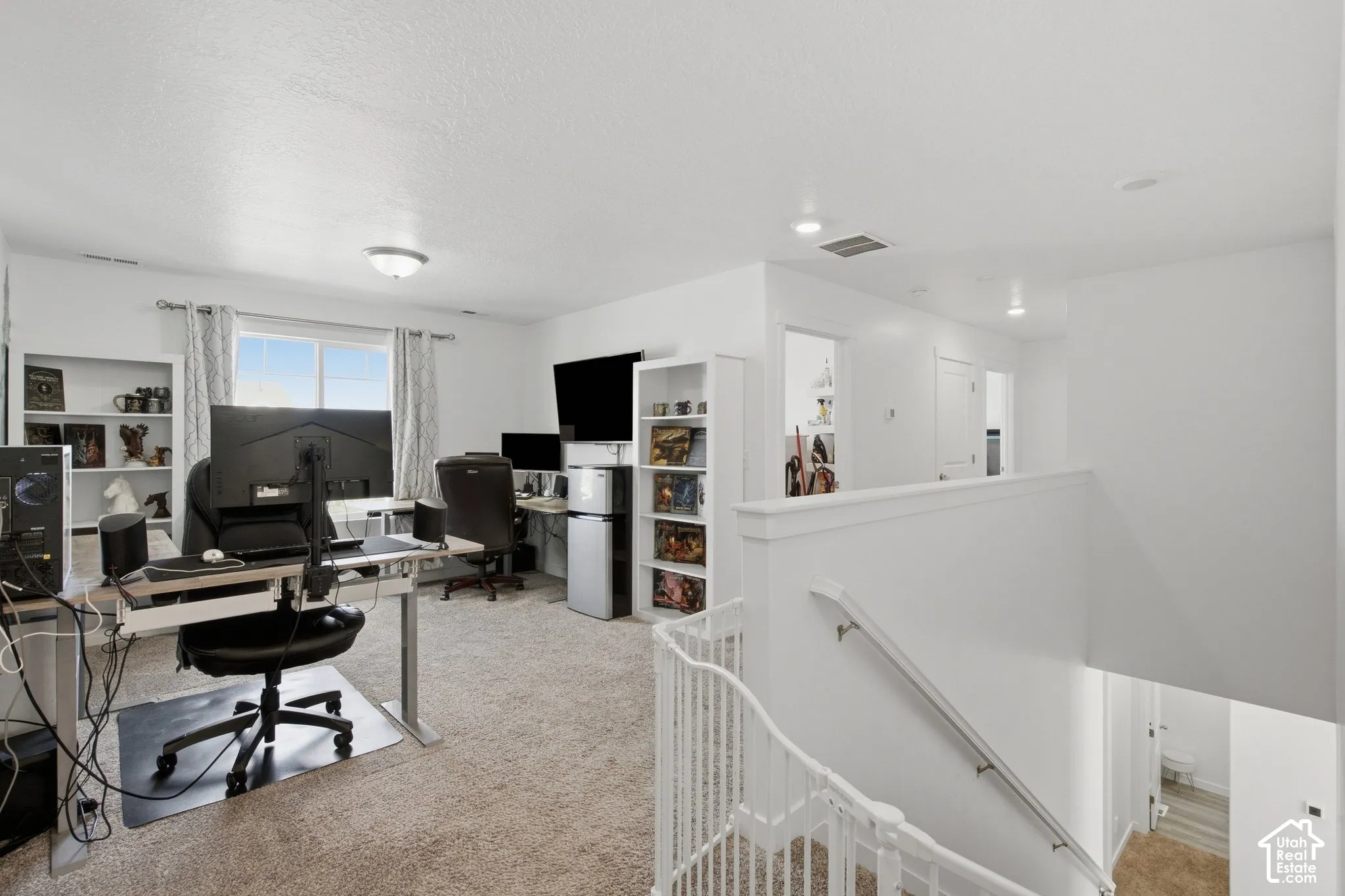 Recessed lighting, built-in shelving, carpet flooring, window with natural light, and a white balustrade with railing