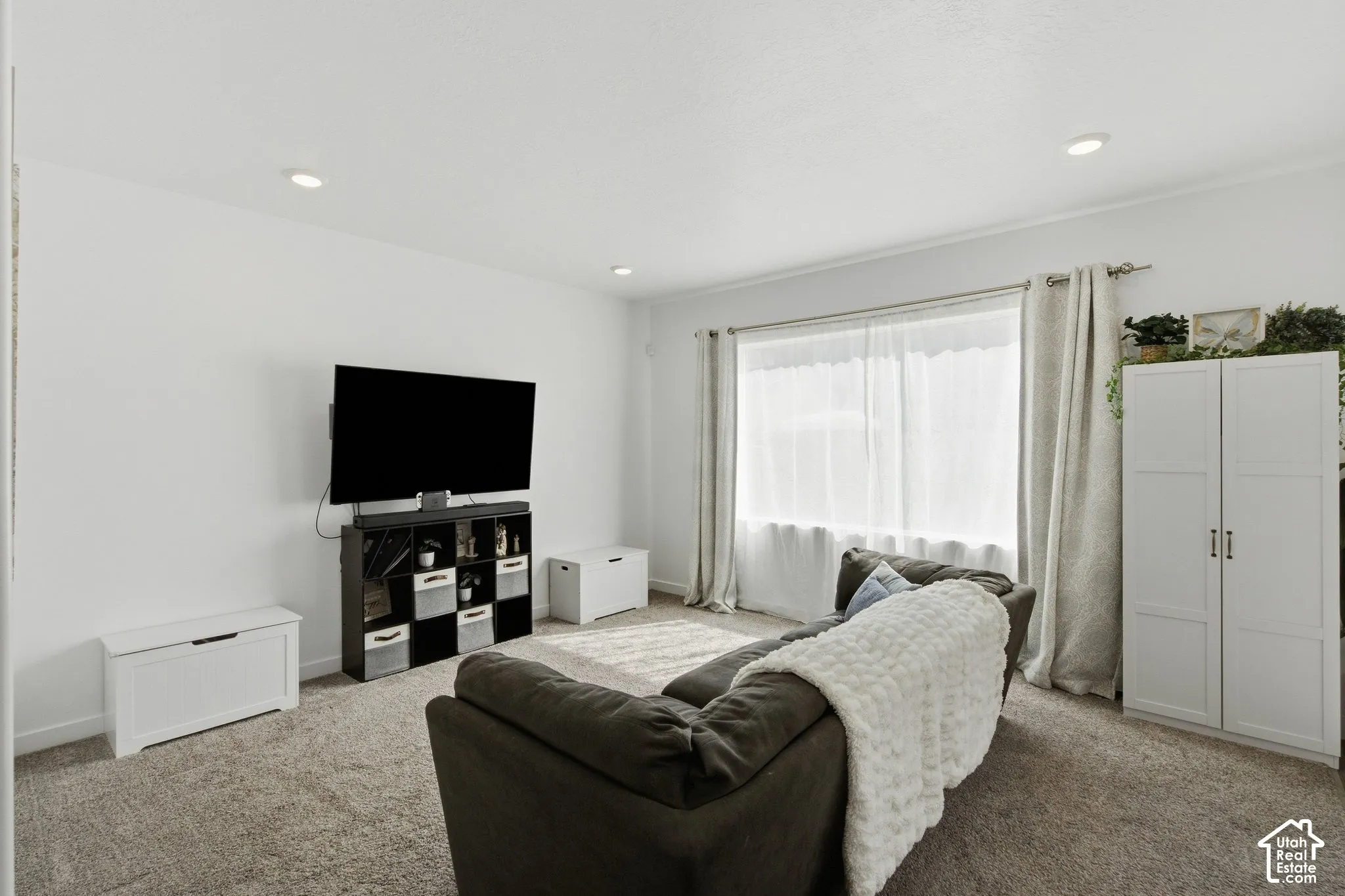 Recessed ceiling lighting, textured wall-to-wall carpeting, window with sheer and blackout curtains, and white built-in cabinetry