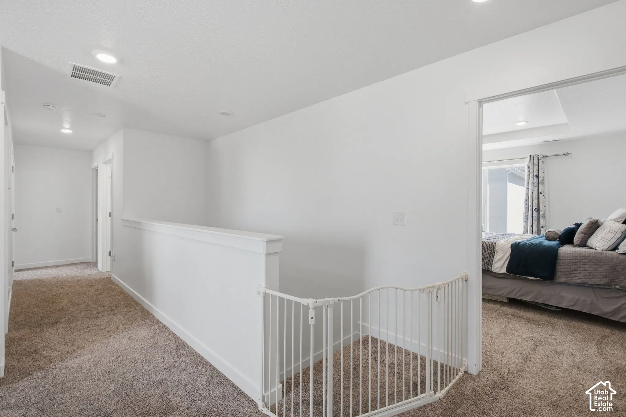 Carpeted hallway featuring white walls, recessed lighting, and a white banister