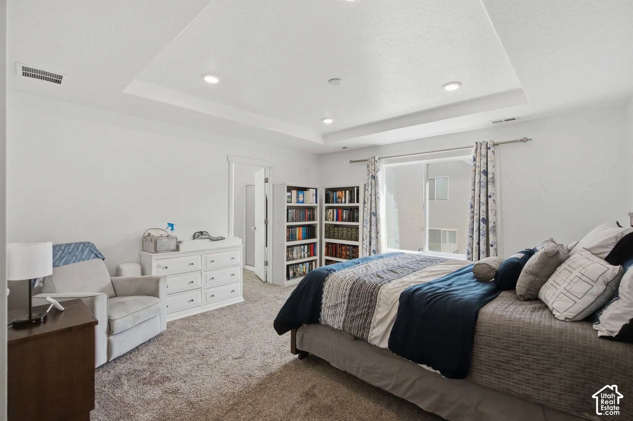 Tray ceiling with recessed lighting, integrated built-in shelving, sliding glass door, and neutral-toned carpeting