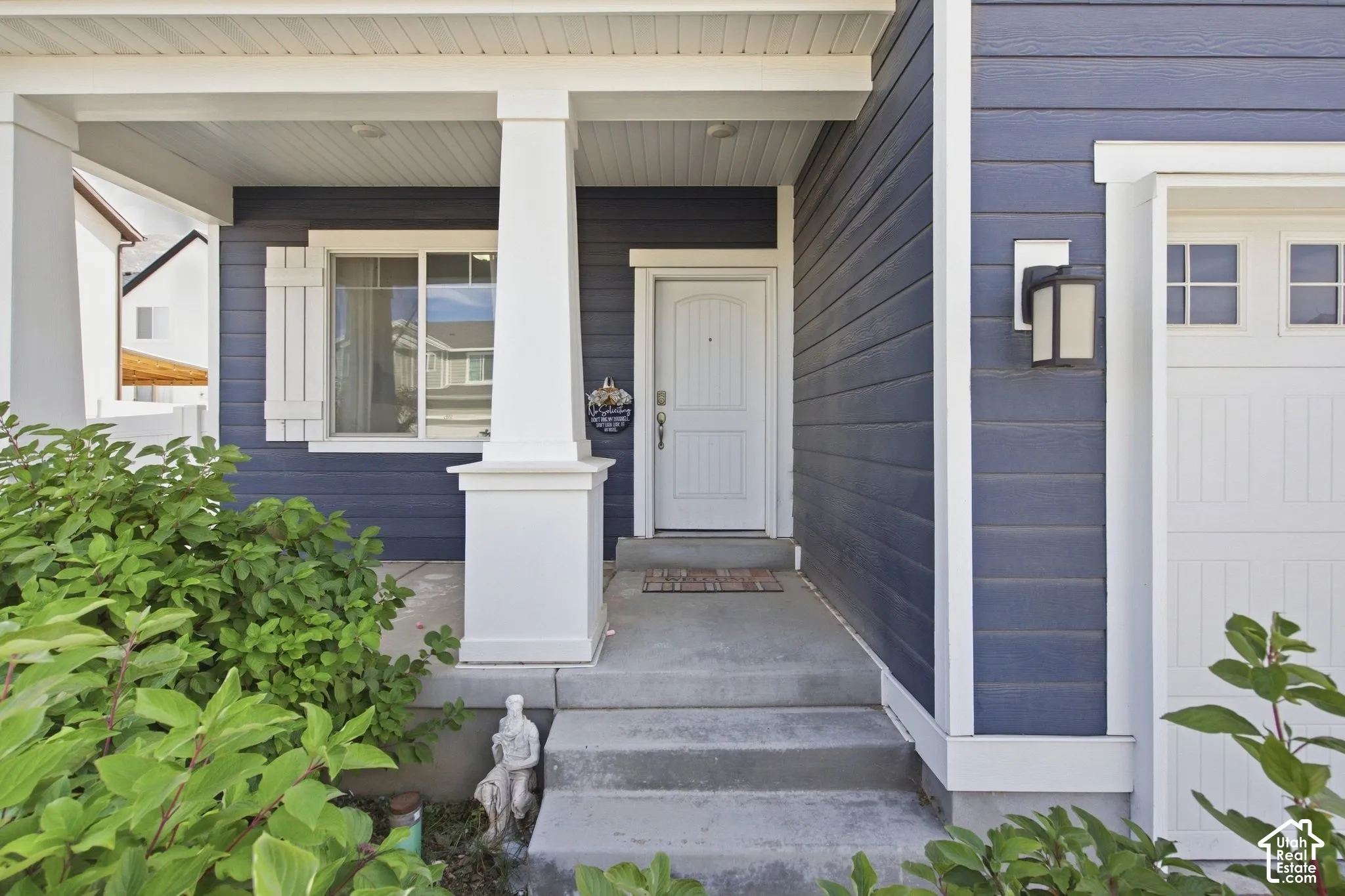 Covered porch entry featuring white columns, a paneled front door, and a built-in outdoor light fixture
