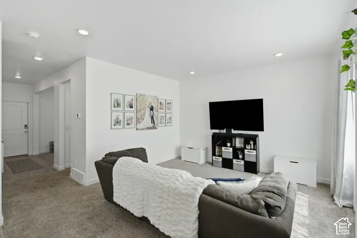 Recessed lighting, light gray carpet flooring, white painted walls, and a white front entry door