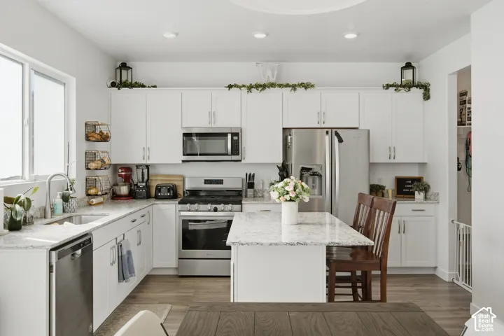 White cabinetry with brushed nickel hardware, stainless steel appliances, a center island with counter seating, light-toned countertops, and wood-finish flooring