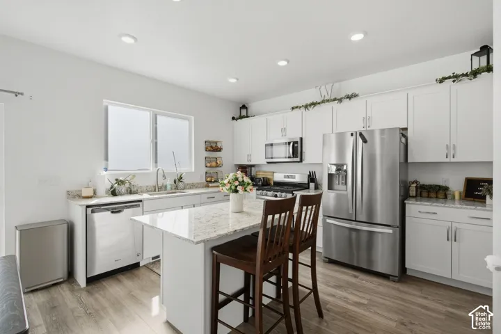 Kitchen featuring white cabinetry, stainless steel appliances, a center island with a stone-finish countertop, recessed lighting, and wood-finish flooring