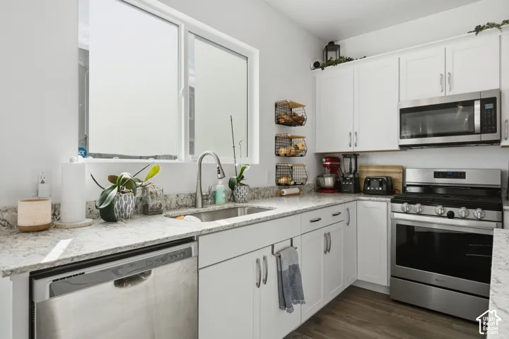Kitchen featuring white cabinetry, light-toned countertops, stainless steel appliances, and wood-finish flooring