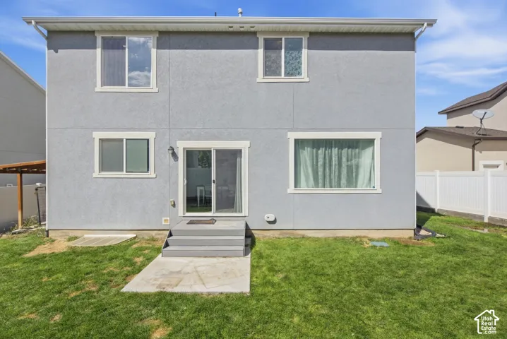 Gray stucco exterior with white trim windows and sliding glass door, leading to a concrete patio and a grassy yard
