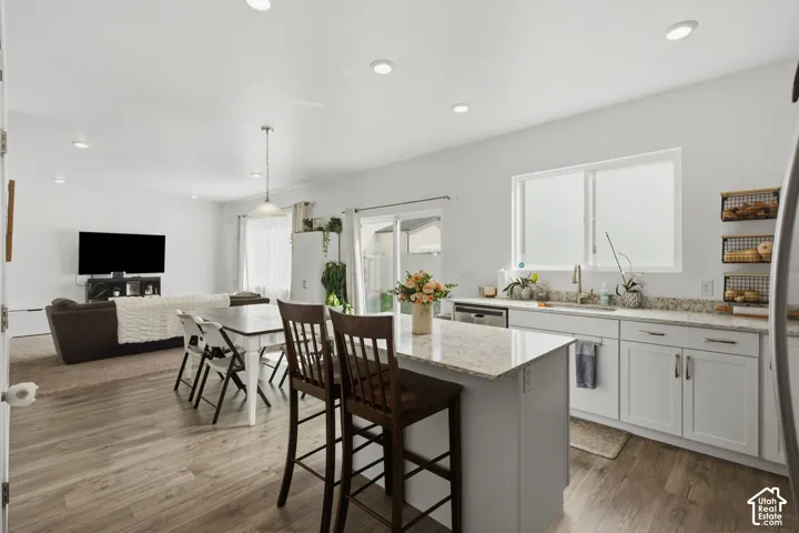 Open-concept kitchen and living area featuring wood-finish flooring, recessed lighting, white cabinetry, and light-toned countertops
