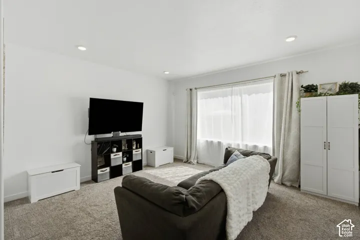 Recessed ceiling lighting, textured wall-to-wall carpeting, window with sheer and blackout curtains, and white built-in cabinetry