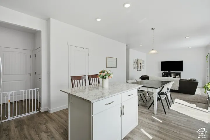 Kitchen island with a light-toned countertop, white cabinetry with silver hardware, and wood-finish flooring