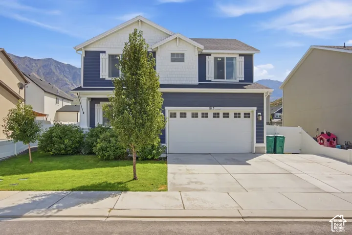 Two-story residence featuring blue siding with white trim, an attached garage, a paved driveway, and a front lawn with established landscaping