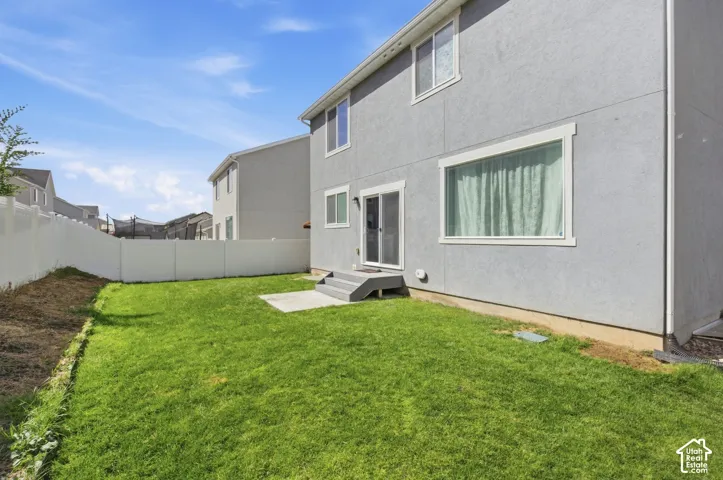 Expansive backyard featuring a green lawn, concrete patio, and white vinyl fencing