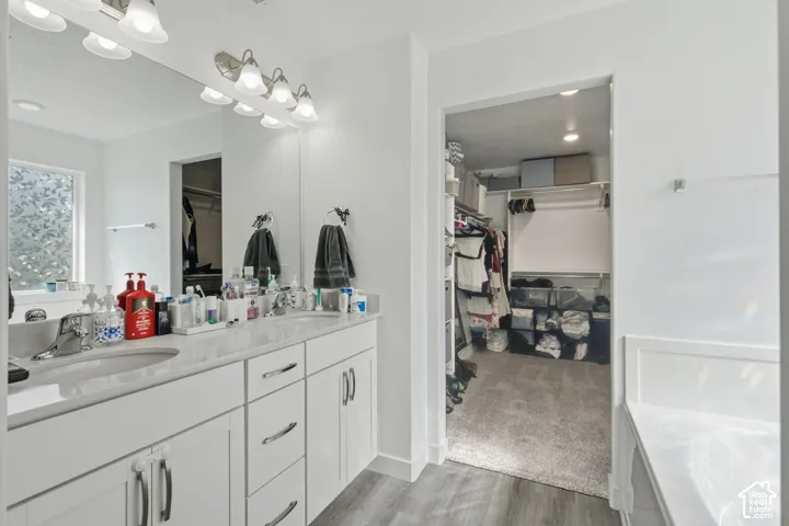 Double vanity with undermount sinks, wall-mounted light fixture, large mirror, and wood-finish flooring