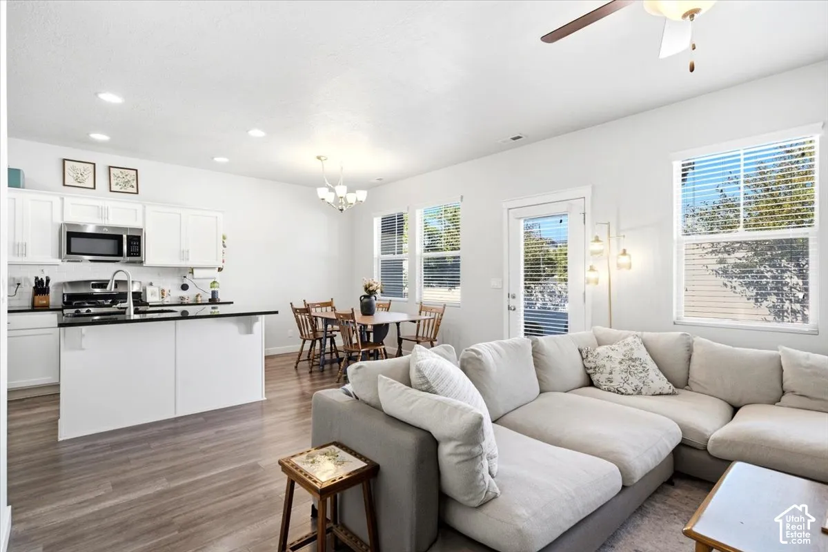Open-concept living area with wood-finish flooring, white cabinetry, stainless steel appliances, and ceiling fan