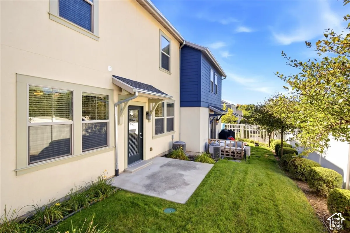 Paved patio area, manicured lawn, established shrubs, and a partial privacy fence